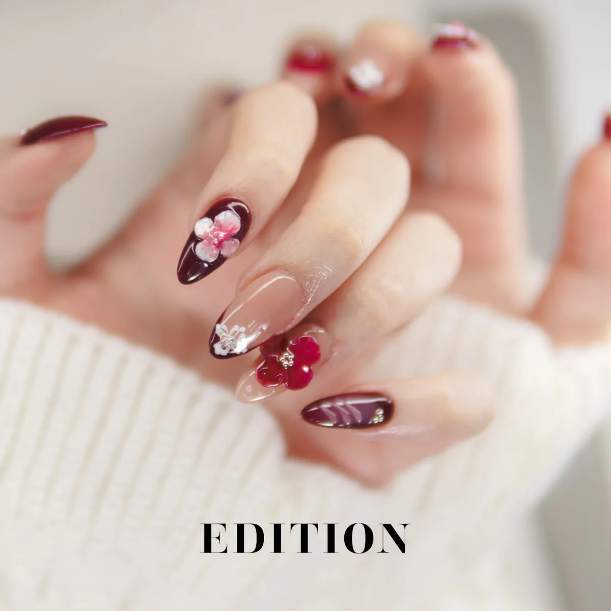 Burgundy almond nails with raised 3D flower art in pink and red, EDITION Salon client work, with the EDITION wordmark