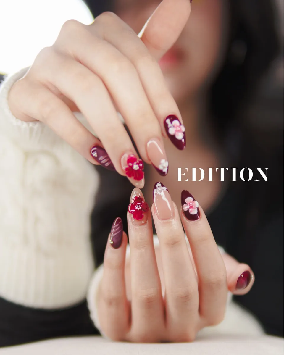 Both hands with long almond nail extensions in burgundy and nude, decorated with raised red and pink flower art, EDITION Salon client work
