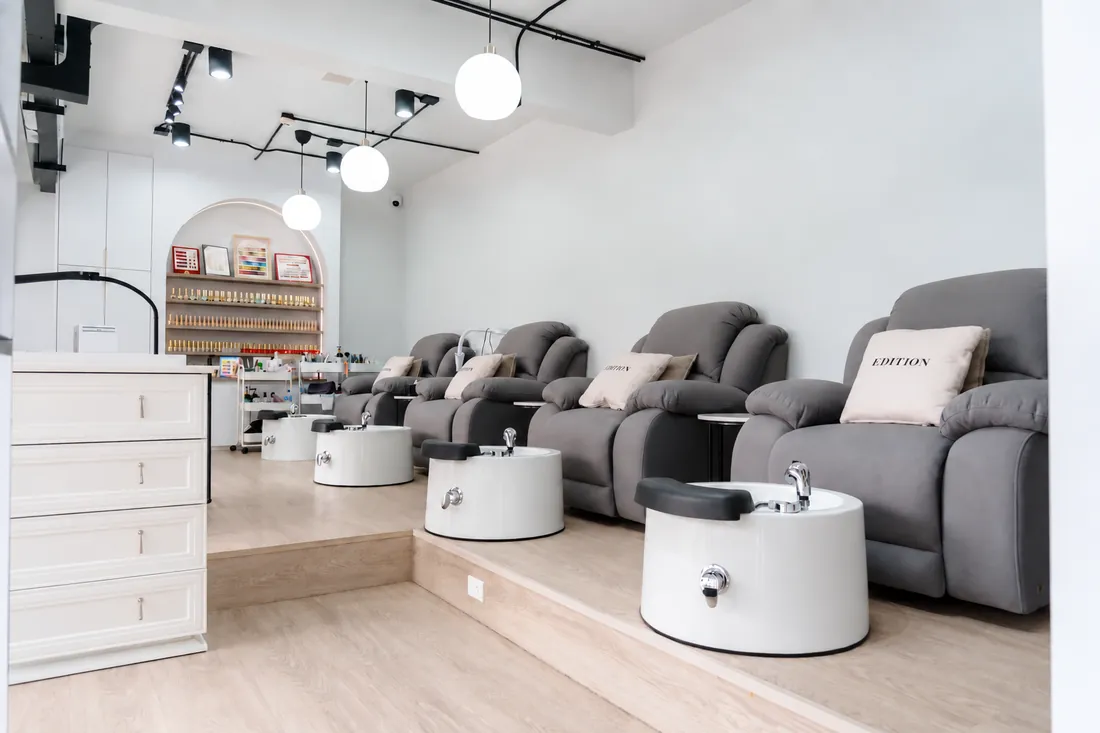 Nail room with grey recliners, pedicure basins and nail polish shelves at EDITION Salon Pattaya