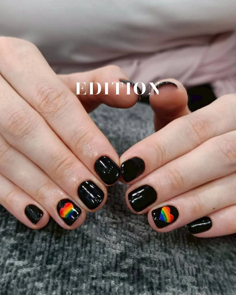 Short natural nails in glossy black gel polish with a rainbow heart on two accent nails, EDITION Salon client work